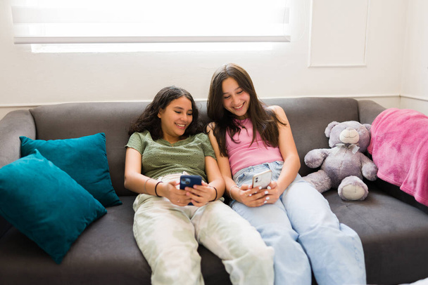 Vrolijk tienermeisje lachen tijdens het sms 'en met haar beste vriendin en met behulp van sociale media op de smartphone, terwijl opknoping out in de slaapkamer - Foto, afbeelding