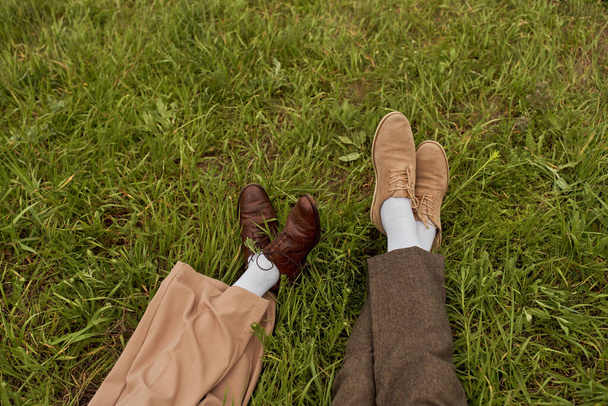 Top kilátás lábak romantikus pár vintage cipő és nadrág ül egymás mellett a füves gyep, stílusos partnerek a vidéki menekülés, romantikus menekülés - Fotó, kép