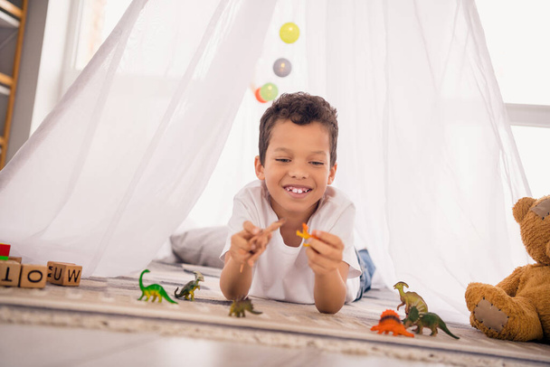 Photo of cute adorable preschool boy in homemade camp playing with animal toys dinosaurs learn about jurassic history in house. - Photo, image