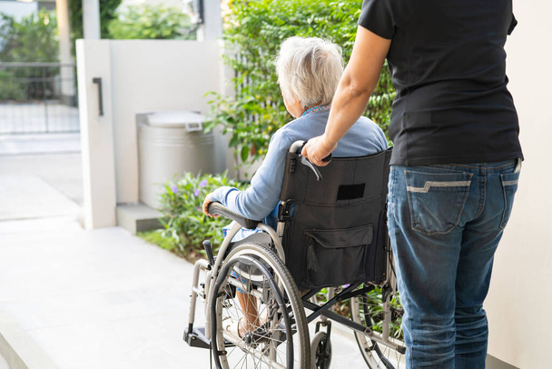 Φροντιστής βοήθεια και φροντίδα Ασιάτισσα ηλικιωμένη γυναίκα ασθενής κάθεται σε αναπηρική καρέκλα ράμπα στο νοσηλευτικό νοσοκομείο, υγιή ισχυρή ιατρική έννοια. - Φωτογραφία, εικόνα