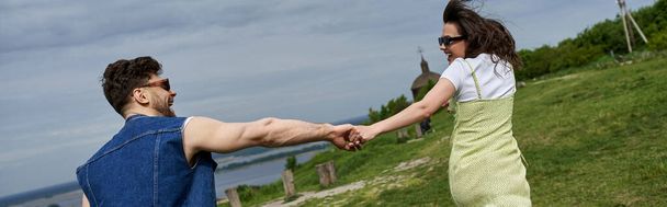 Güneş gözlüklü neşeli esmer kadın ve sakallı erkek arkadaşının elini tutarken taşra gezginliği ve aşk konsepti, pankart  - Fotoğraf, Görsel