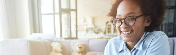 Menina adolescente de raça mista feliz em óculos sorrindo ao fazer lição de casa usando laptop, estudando na sala de estar em casa durante a quarentena. Conceito de ensino em casa e à distância - Foto, Imagem