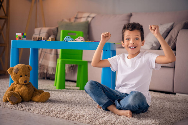 Photo of excited kid boy sit floor comfort cozy play room raise fists up wait for best family parents. - Fotó, kép