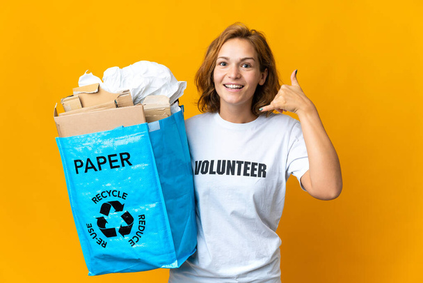 電話のジェスチャーを作るリサイクルのために紙でいっぱいのリサイクルバッグを持っている若いグルジアの女の子。サインを呼んでくれ - 写真・画像
