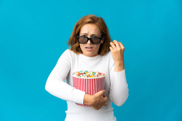 Giovane donna georgiana isolato su sfondo blu con occhiali 3d e tenendo un grande secchio di popcorn - Foto, immagini