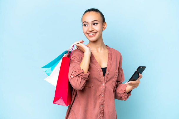 Young Arab woman isolated on blue background holding shopping bags and a mobile phone - Foto, Bild
