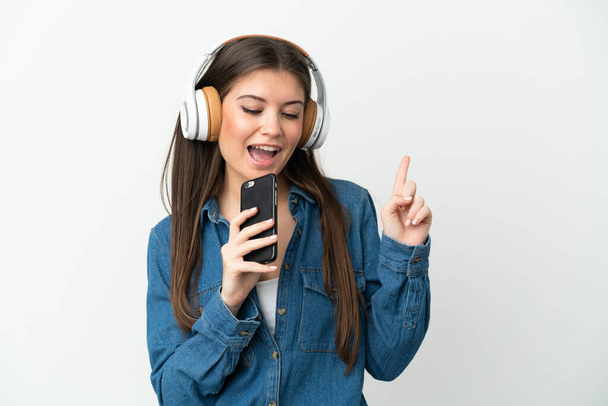 Young caucasian woman isolated on white background listening music with a mobile and singing - 写真・画像