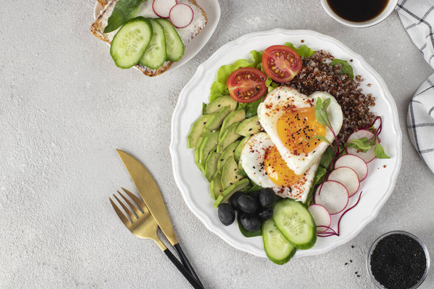 Healthy romantic breakfast - heart-shaped fried eggs served with avocado, spinach, quinoa, cherry tomatoes, radish, cucumber and olives on white plate, Top view - Foto, Bild