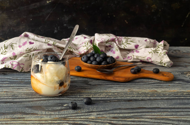 Het dessert. Heerlijk ijs in een glas met siroop en bosbessen op een houten tafel close-up - Foto, afbeelding