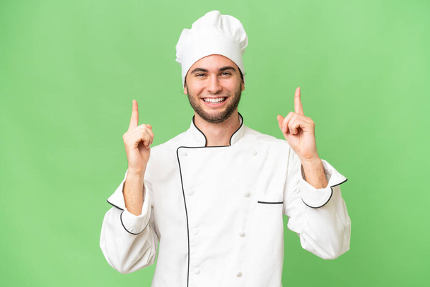 jovem bonito chef homem sobre isolado fundo apontando para cima uma grande ideia - Foto, Imagem