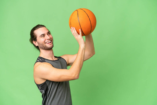Joven hombre guapo aislado en fondo de croma verde jugando baloncesto - Foto, imagen