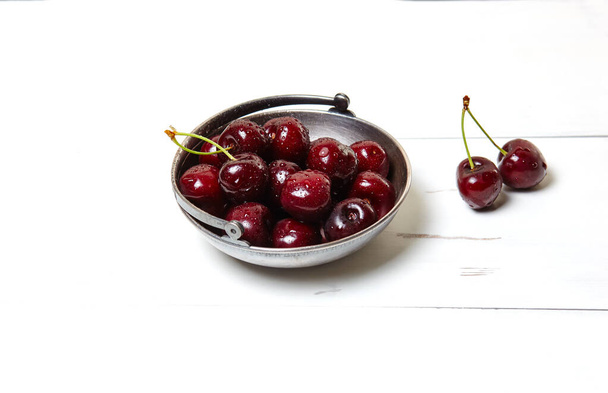 Sweet cherries in a metal bowl on wooden background, closeup. Fresh ripe sweet cherries in a bowl with droplets of water - Foto, afbeelding
