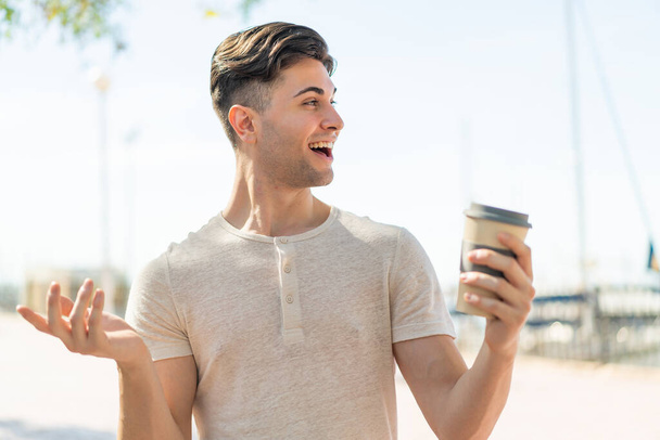 Jovem homem bonito segurando um café take away ao ar livre com expressão facial surpresa - Foto, Imagem