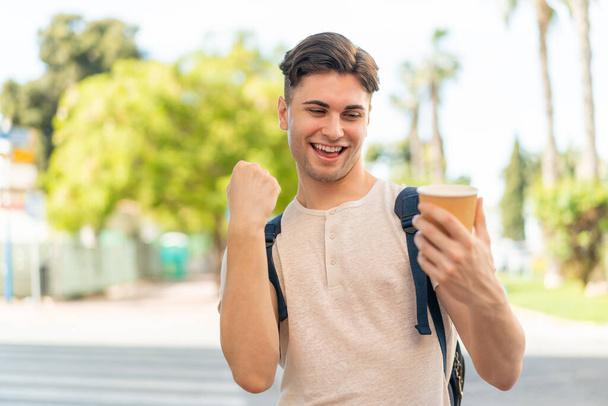 Fiatal jóképű férfi, aki kávét visz magával a szabadban, hogy megünnepelje a győzelmet. - Fotó, kép