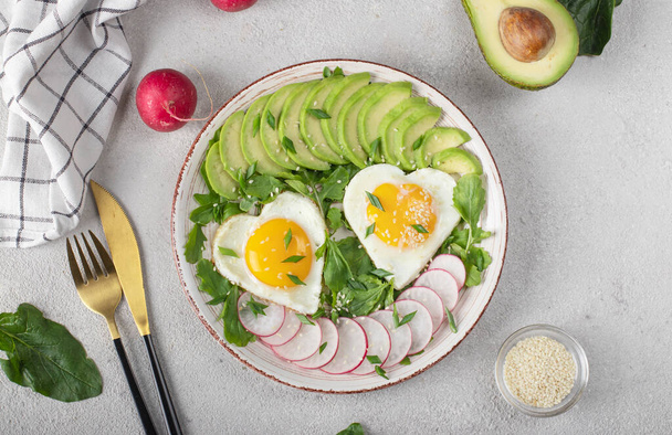Υγιεινό ρομαντικό πρωινό - τηγανητά αυγά σε σχήμα καρδιάς σερβιρισμένα με αβοκάντο και ραπανάκι - Φωτογραφία, εικόνα