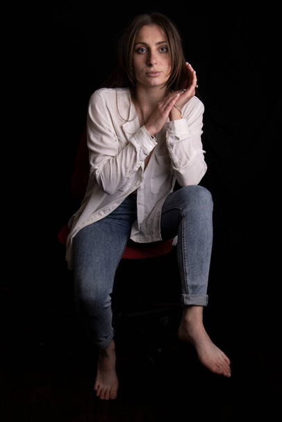 Beautiful young girl in a white shirt and jeans on a black background. - Fotó, kép