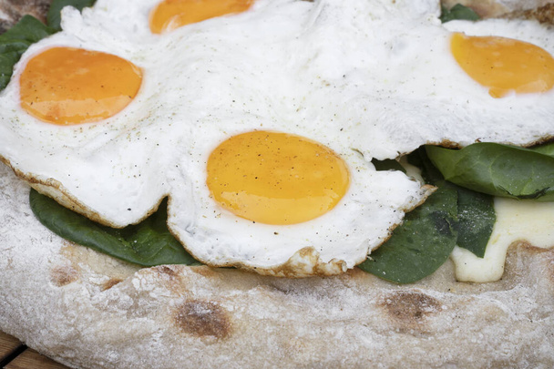 Food background. Closeup view of a pizza with mozzarella cheese, spinach and fried eggs, on the wooden table. - Photo, image
