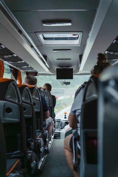Uvnitř autobusu s řadami sedadel pro cestující během deště, kapkami deště na čelní sklo osobního autobusu, přístrojovou deskou řidiče autobusu, turistickou cestou na zataženo - Fotografie, Obrázek
