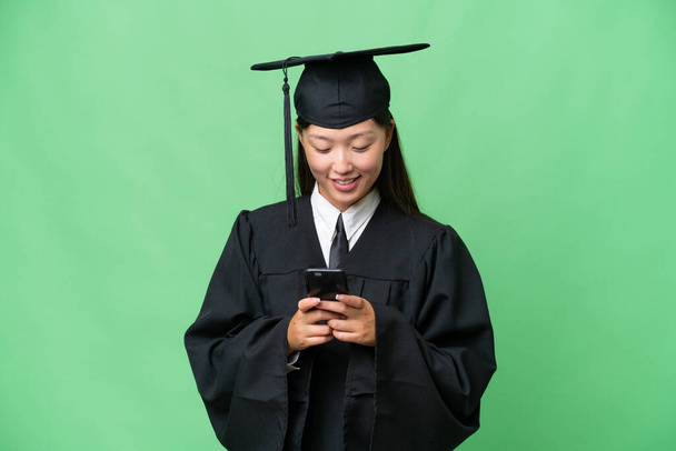 Jovem universitária graduada mulher asiática sobre fundo isolado enviando uma mensagem com o celular - Foto, Imagem