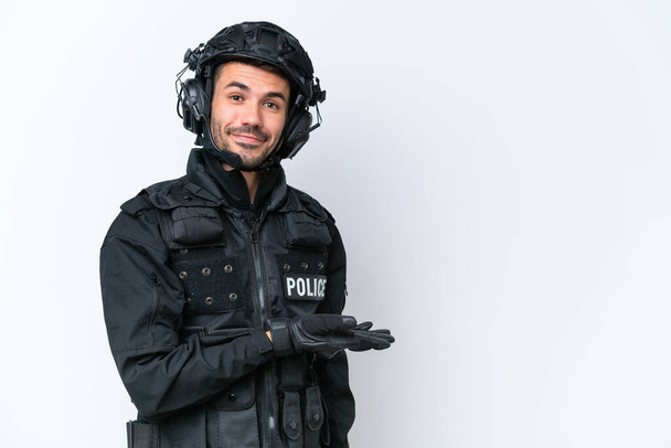 Jeune homme SWAT caucasien isolé sur fond blanc présentant une idée tout en regardant souriant vers - Photo, image