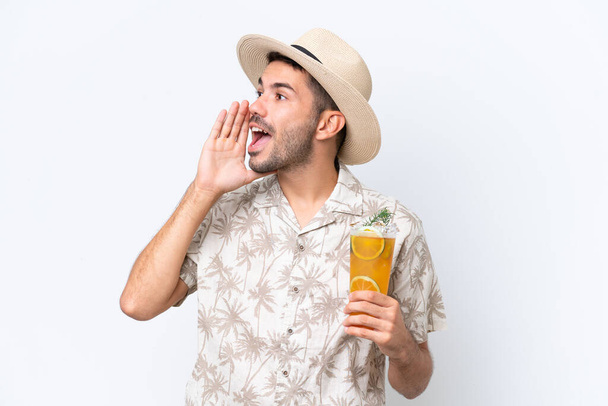 Jonge blanke man met een cocktail geïsoleerd op witte achtergrond schreeuwen met de mond wijd open aan de zijkant - Foto, afbeelding