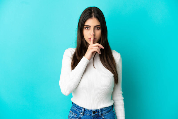 Young caucasian woman isolated on blue background showing a sign of silence gesture putting finger in mouth - Foto, imagen