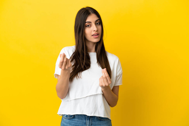 Young caucasian woman isolated on yellow background making money gesture but is ruined - Фото, изображение
