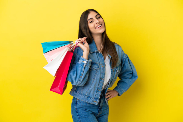 Young caucasian woman isolated on blue background holding shopping bags and smiling - Foto, Bild