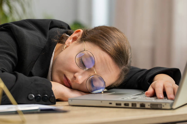 Donna d'affari caucasica assonnata annoiata in lavoratore di occhiali che lavora a computer portatile che si appoggia a mano che si addormenta a ufficio. Stanco stanco freelance maniaco del lavoro ragazza. Occupazione, senza lavoro - Foto, immagini