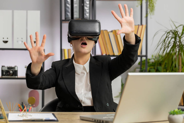 Donna d'affari che utilizza la realtà virtuale tecnologia futuristica VR app casco auricolare per la simulazione 3D 360 video sul posto di lavoro ufficio moderno. Emozionata manager ragazza freelance. Telecomando remoto lavoro online - Foto, immagini