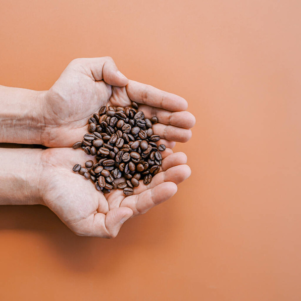 茶色の背景にコーヒー豆を手に持ち  - 写真・画像