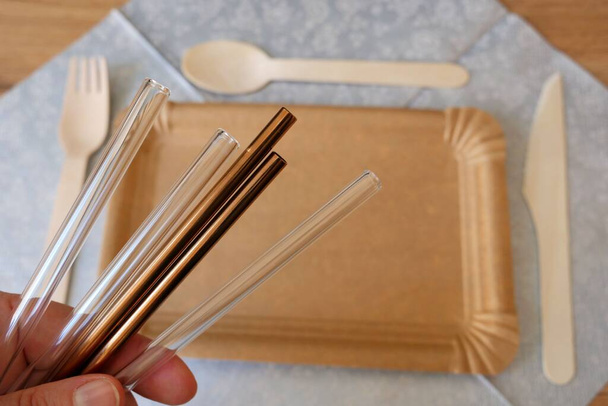 Copper and glass reusable drinking straws in a hand. Picnic wooden cutlery in the background. - Fotó, kép