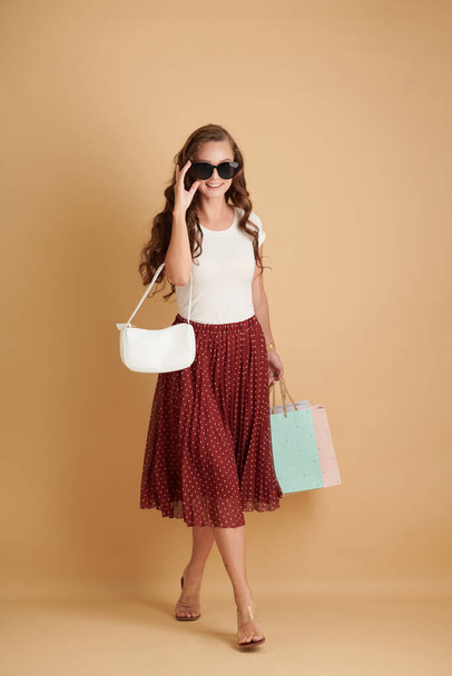 Uśmiechnięta młoda kobieta z torbami na zakupy w ręku i okularami przeciwsłonecznymi - Zdjęcie, obraz