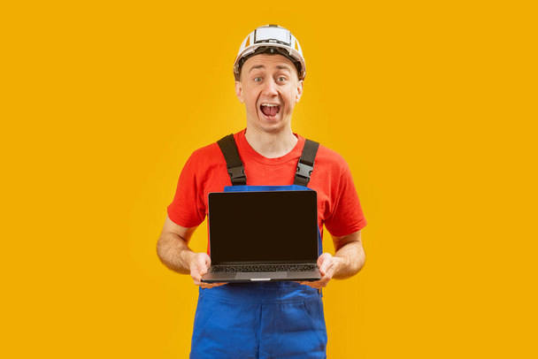 Schöner männlicher Vorarbeiter mit Laptop und leerem Bildschirm auf gelbem Hintergrund. Kopierraum, Attrappe - Foto, Bild