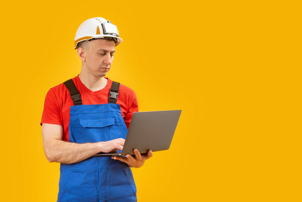 Férfi ipari mérnök vagy munkás áll laptop sárga háttér fotó stúdió. Fénymásolási hely - Fotó, kép