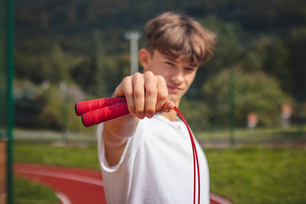 陸上競技場を持つ茶色の髪の少年は、耐久性を向上させるための最良のツールの一つとしてジャンプロープを促進します,ジャンプ力. - 写真・画像
