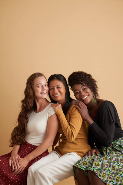 Studio πορτρέτο των χαρούμενων νεαρών γυναικών φίλους κλίνει το ένα πάνω στο άλλο κατά τη φωτογράφηση στο στούντιο - Φωτογραφία, εικόνα