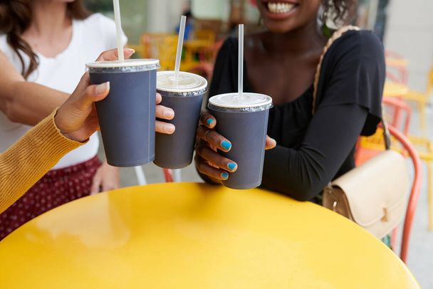 Zbliżenie obrazu przyjaciółek brzęczących plastikowymi szklankami z napojami bezalkoholowymi nad stołem kawiarni - Zdjęcie, obraz