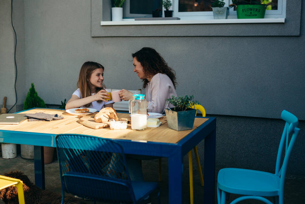 Mother and daughter clinking glasses during breakfast. - Fotografie, Obrázek