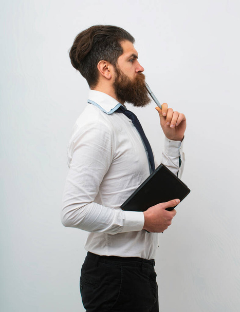 Concentrated man with pen in his mouth. Male with notepad for writing. Businessman holds notepad and pen - Фото, изображение