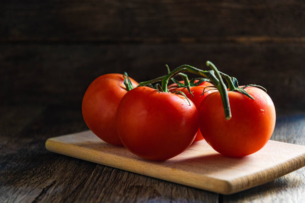 Um ramo de tomates maduros em uma tábua de corte na cozinha. - Foto, Imagem