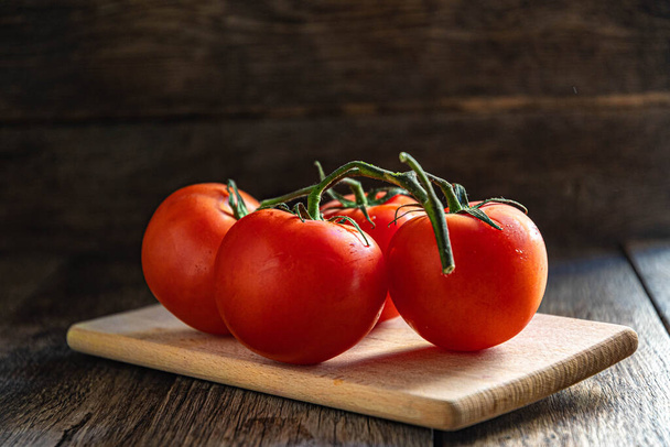 Um ramo de tomates maduros em uma tábua de corte na cozinha. - Foto, Imagem