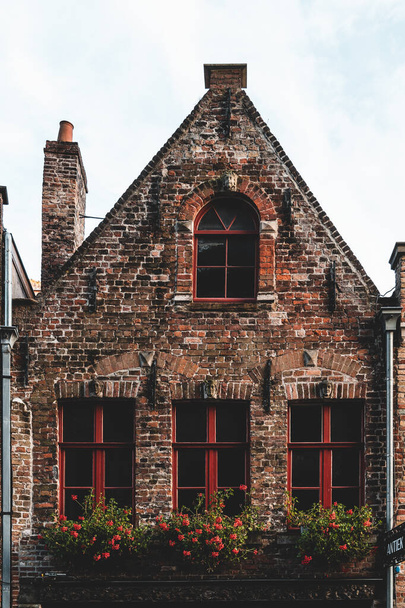 An aged red wooden window adds character to an orange brick house, exuding charm and a sense of history. - 写真・画像
