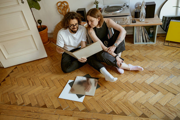 Couple familial assis sur le sol et écoutant de la musique sur un lecteur vinyle avec différents disques - Photo, image