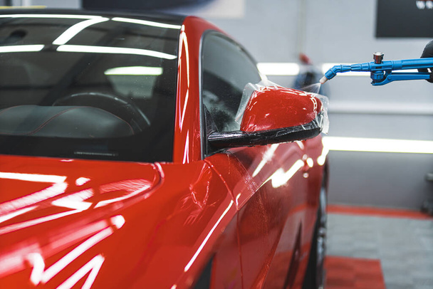 Installation process of PPF - paint protective foil - onto a side mirror of a red sports car. Indoor car detailing studio shot. High quality photo - Foto, Imagen