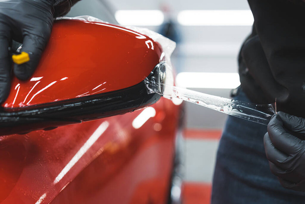 Extreme close seup shot of professional car detailing expert applying or removing transparent foil from a red car. Размытое прошлое. Высокое качество фото - Фото, изображение