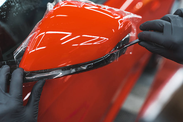 Expert en gants de protection noirs appliquant une pellicule de vinyle de voiture délicatement transparente sur un miroir latéral d'une voiture de sport rouge. Gros plan. Photo de haute qualité - Photo, image