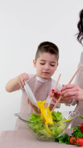 mom teaches son to cook salad boy adds yellow pepper glass plate learns delicious healthy vegetarian food vitamins benefits family leisure white background advertising  - Footage, Video