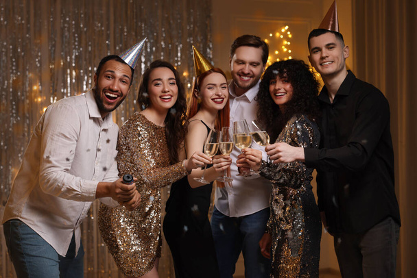 Happy friends clinking glasses of sparkling wine at birthday party indoors - 写真・画像