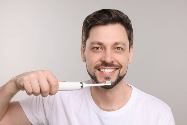 Happy man holding electric toothbrush on light grey background - Photo, Image